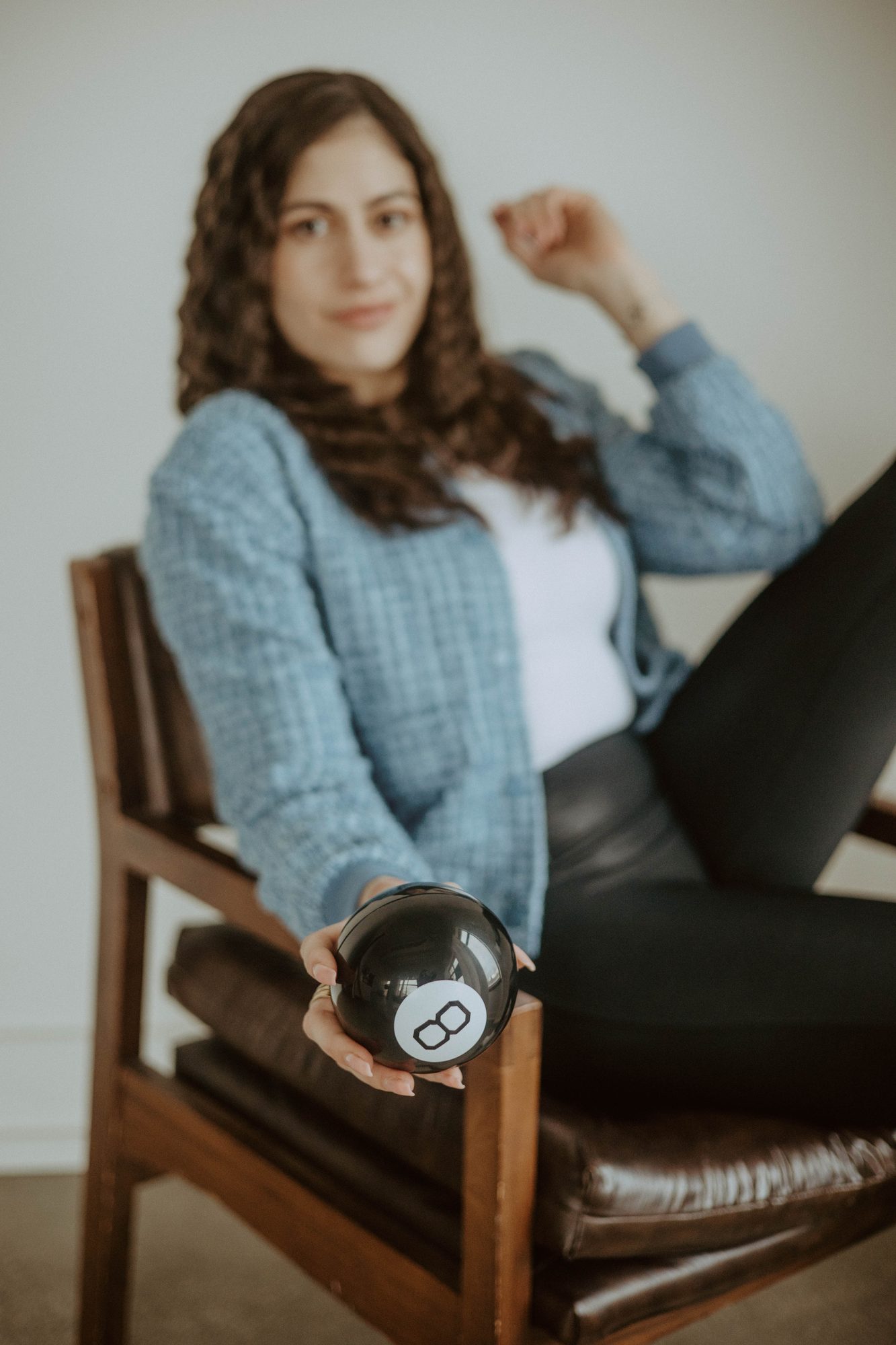 A Magic 8 Ball held in focus while Natalie sits beyond it.